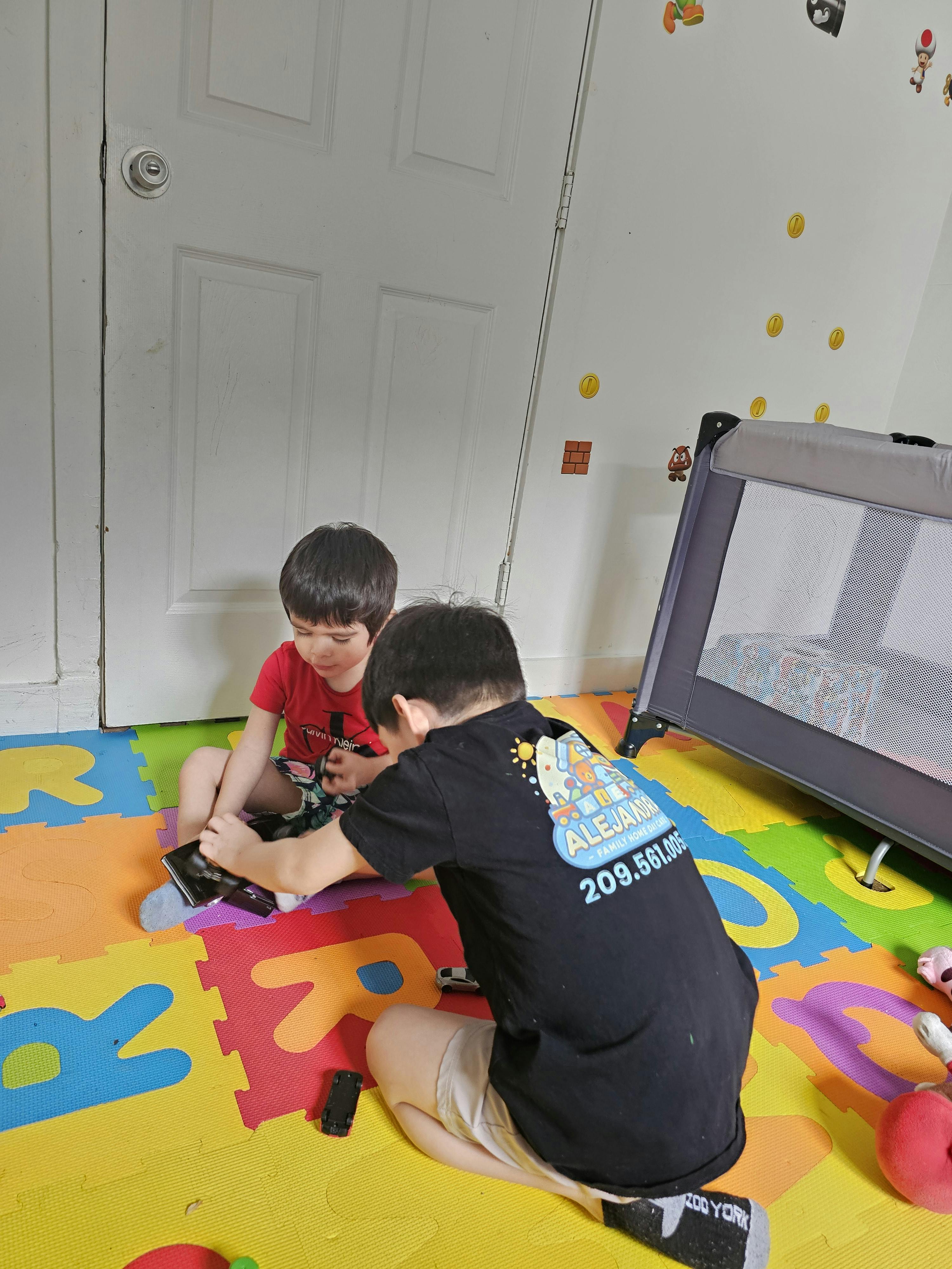 Two children on a colorful mat playing with toy cars