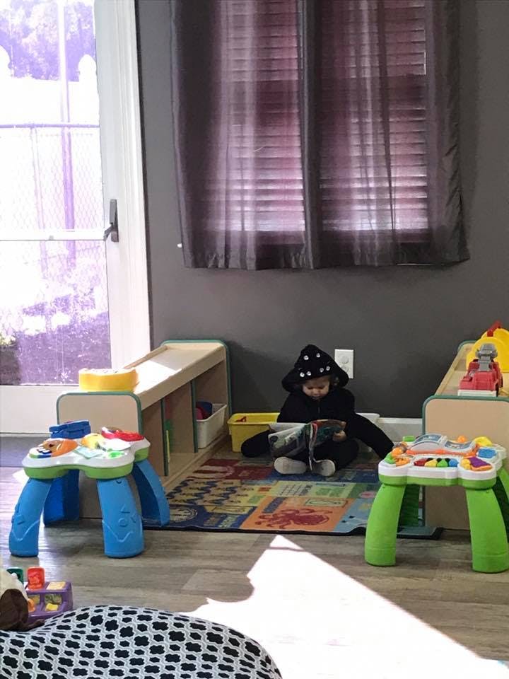 Child in a hooded outfit sitting on a rug with toys