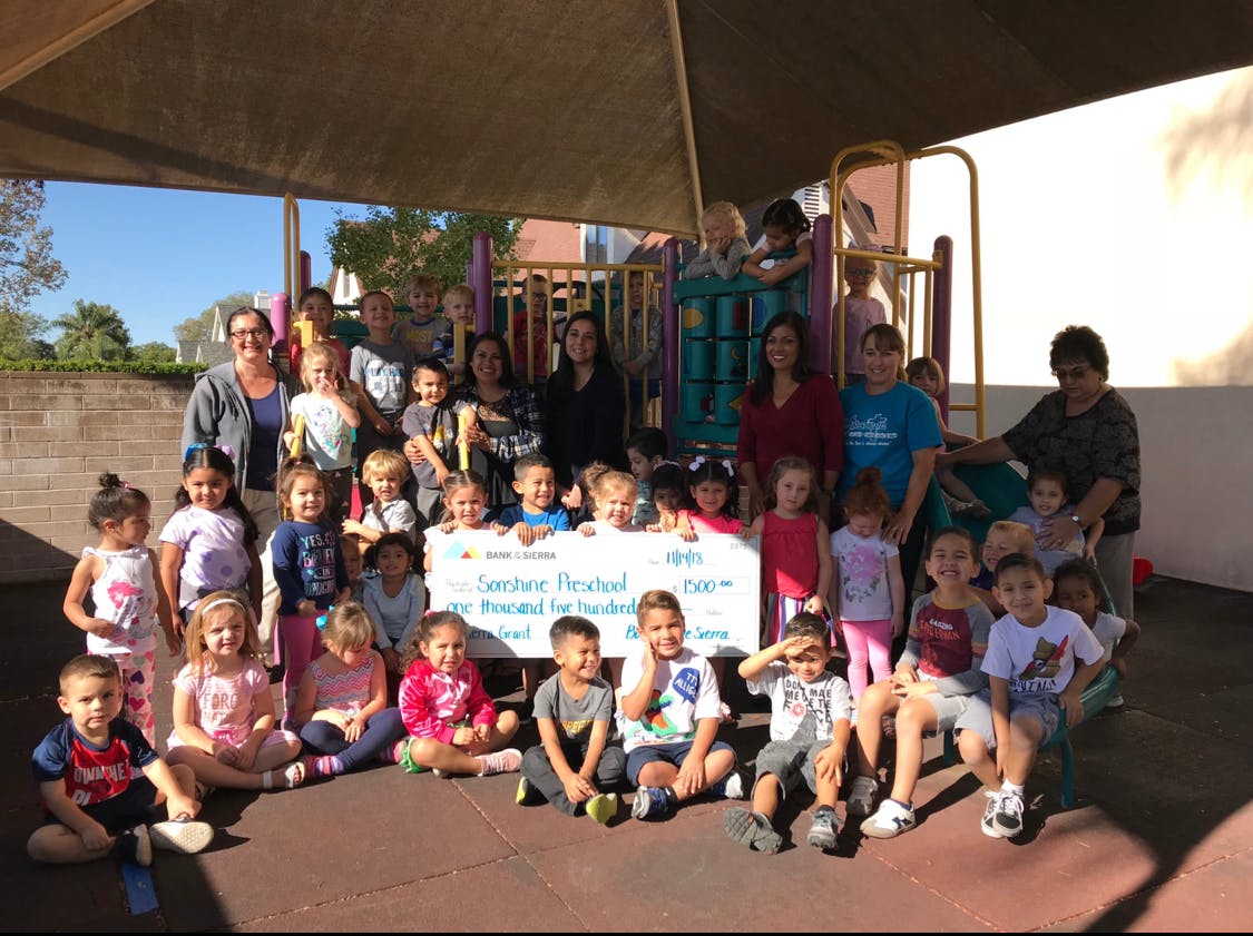 Adults and children holding a large check on a playground