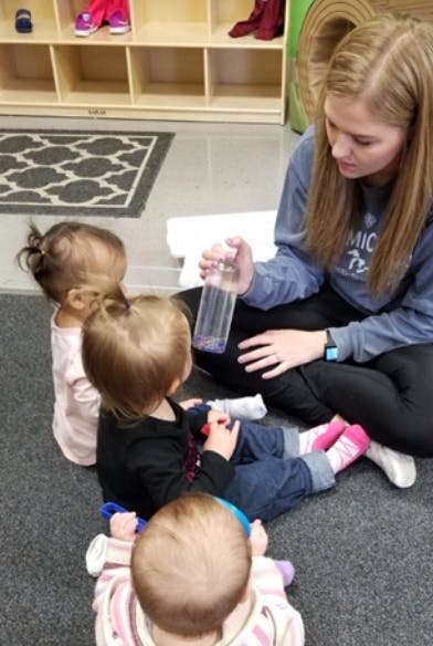 Person holding a bottle for three children sitting on the floor
