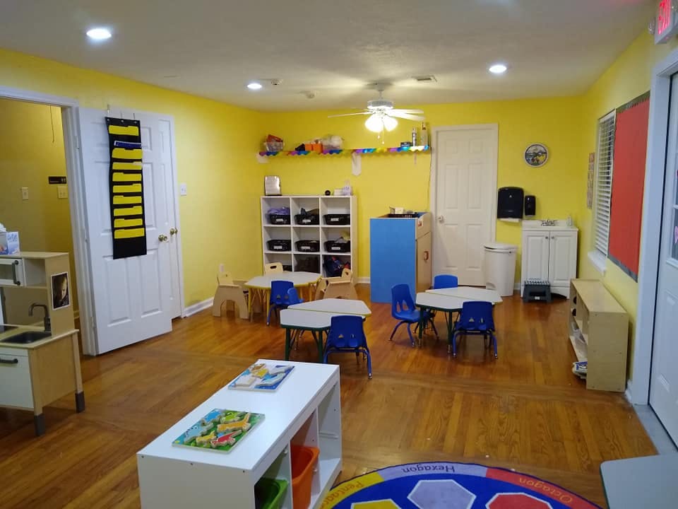Classroom with small tables and chairs, shelves, and yellow walls