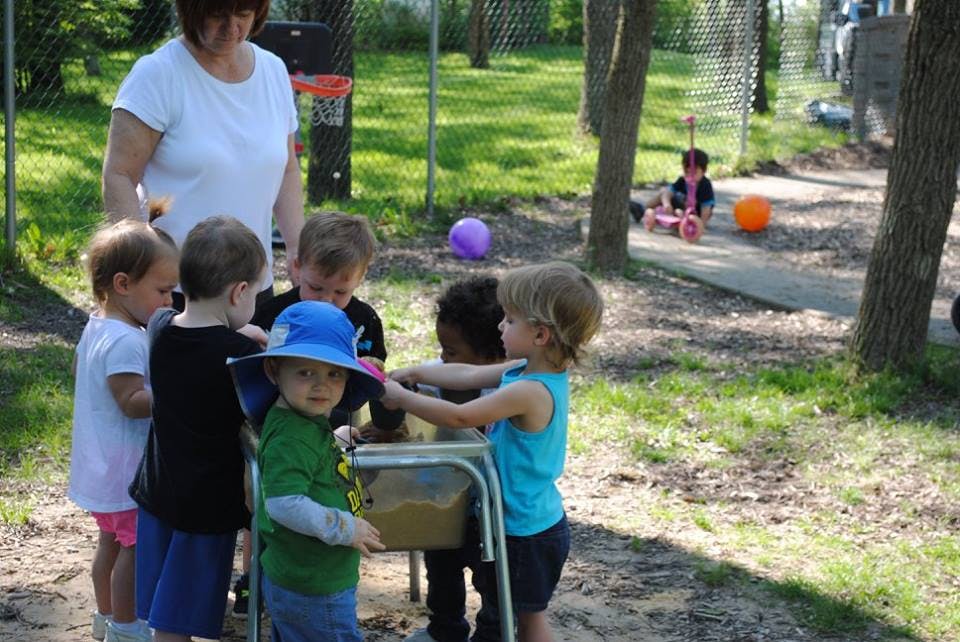 Adult and children gathered around a play table outdoors