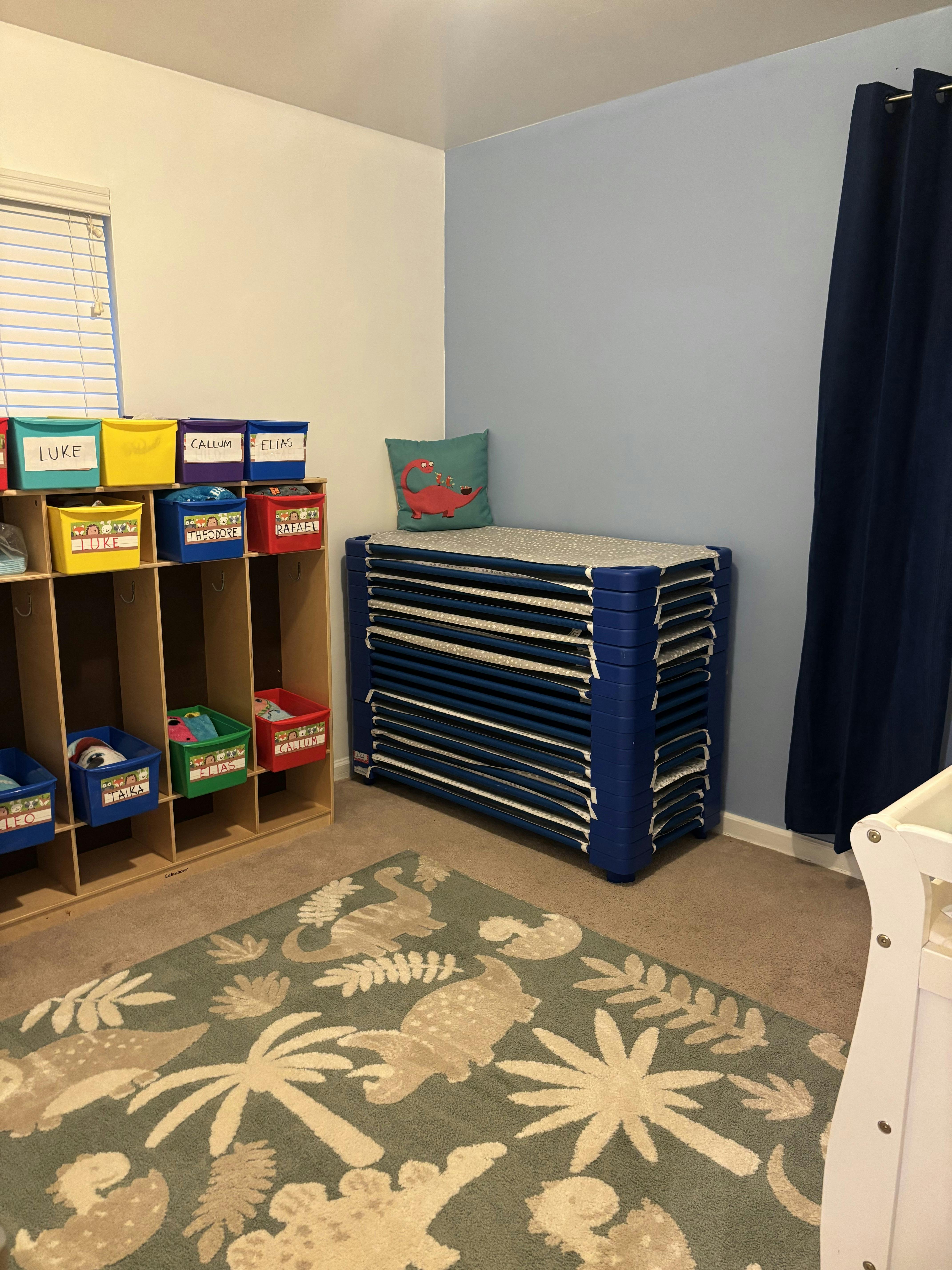 Cubby storage with named bins and a stack of blue cots in a room