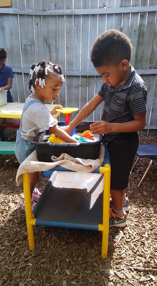 Two children playing with toys in a water table outdoors