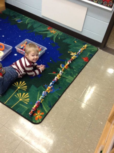 Child lying on a rug with building blocks, looking at the camera