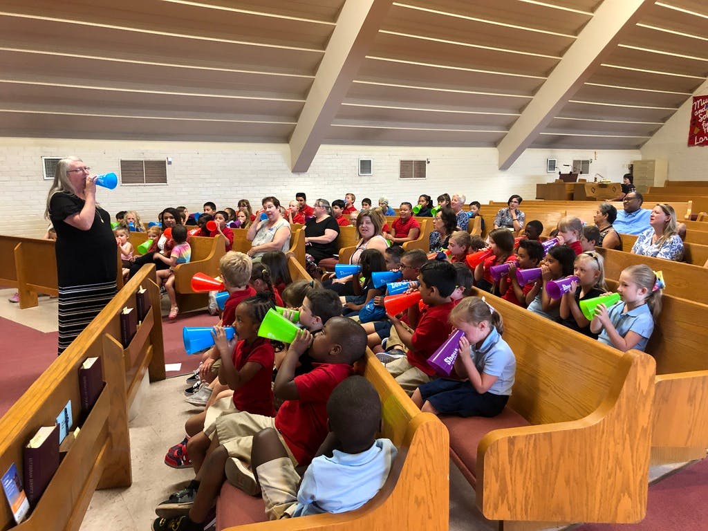 Person speaking into a megaphone to a group of children and adults in pews