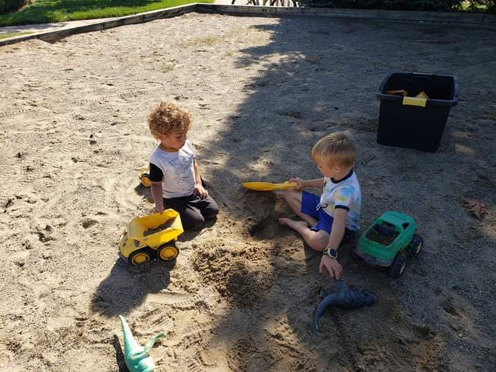 Two children playing in a sandbox with toy trucks and shovels