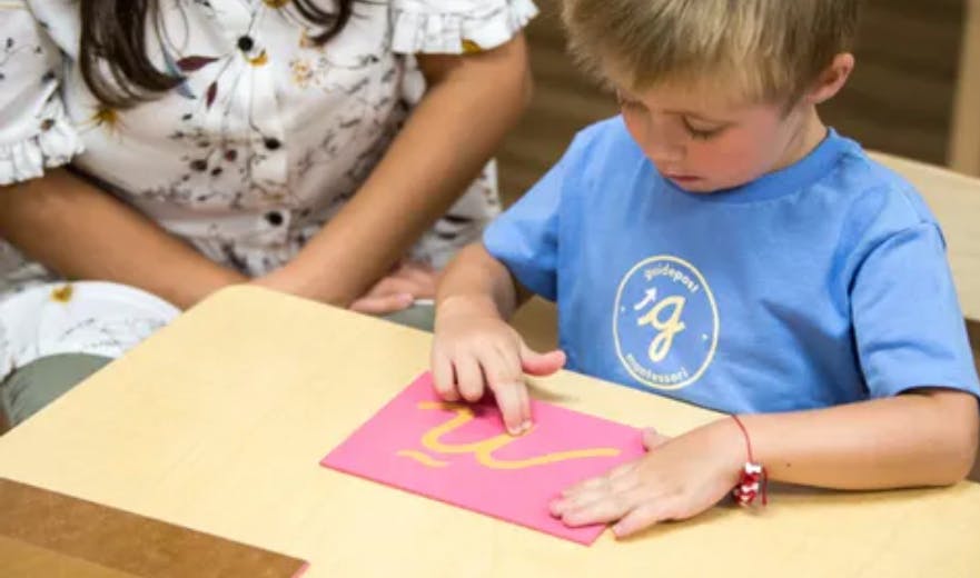 Child tracing a letter on a pink card at a desk