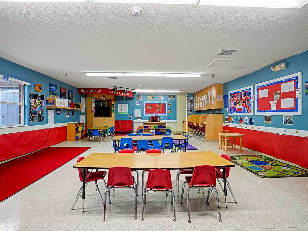 Empty classroom with small tables and chairs, bulletin boards, and red wainscoting