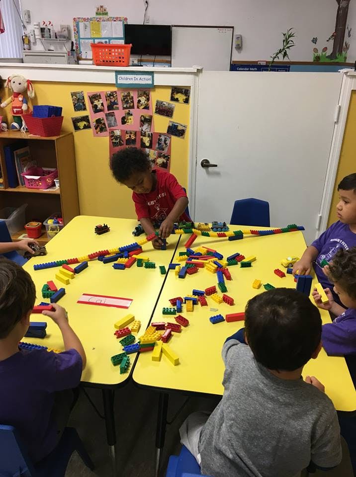 Children playing with colorful building blocks at a yellow table in a classroom