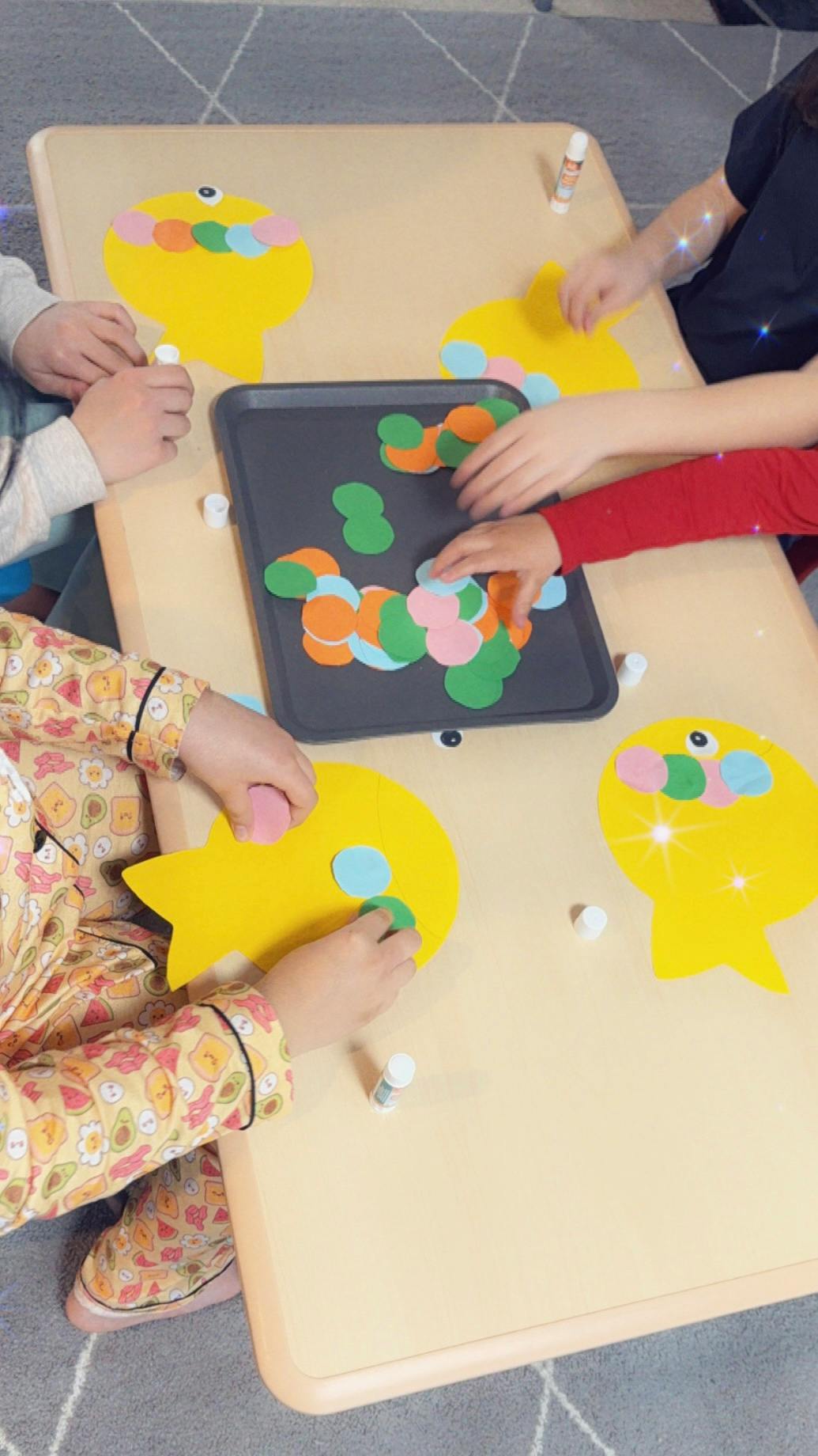Children's hands crafting with yellow paper cutouts and colorful circles