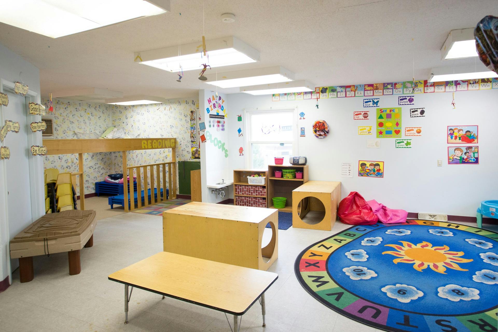 Empty classroom with small tables, chairs, and a colorful rug