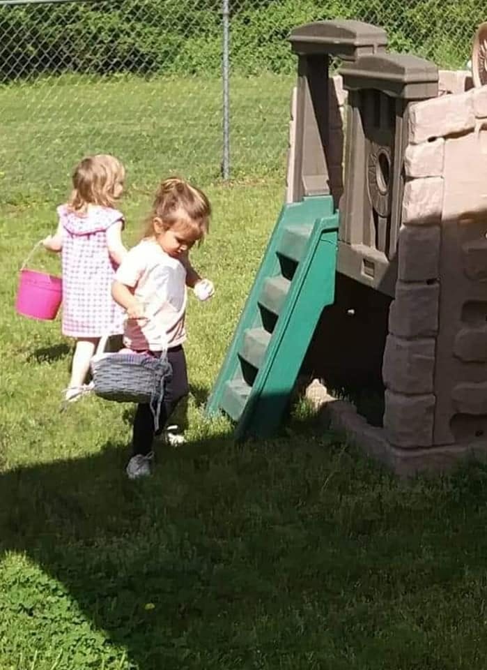 Two children with baskets walking on grass near a play structure