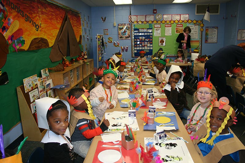 Children in costumes sitting at a long table in a classroom