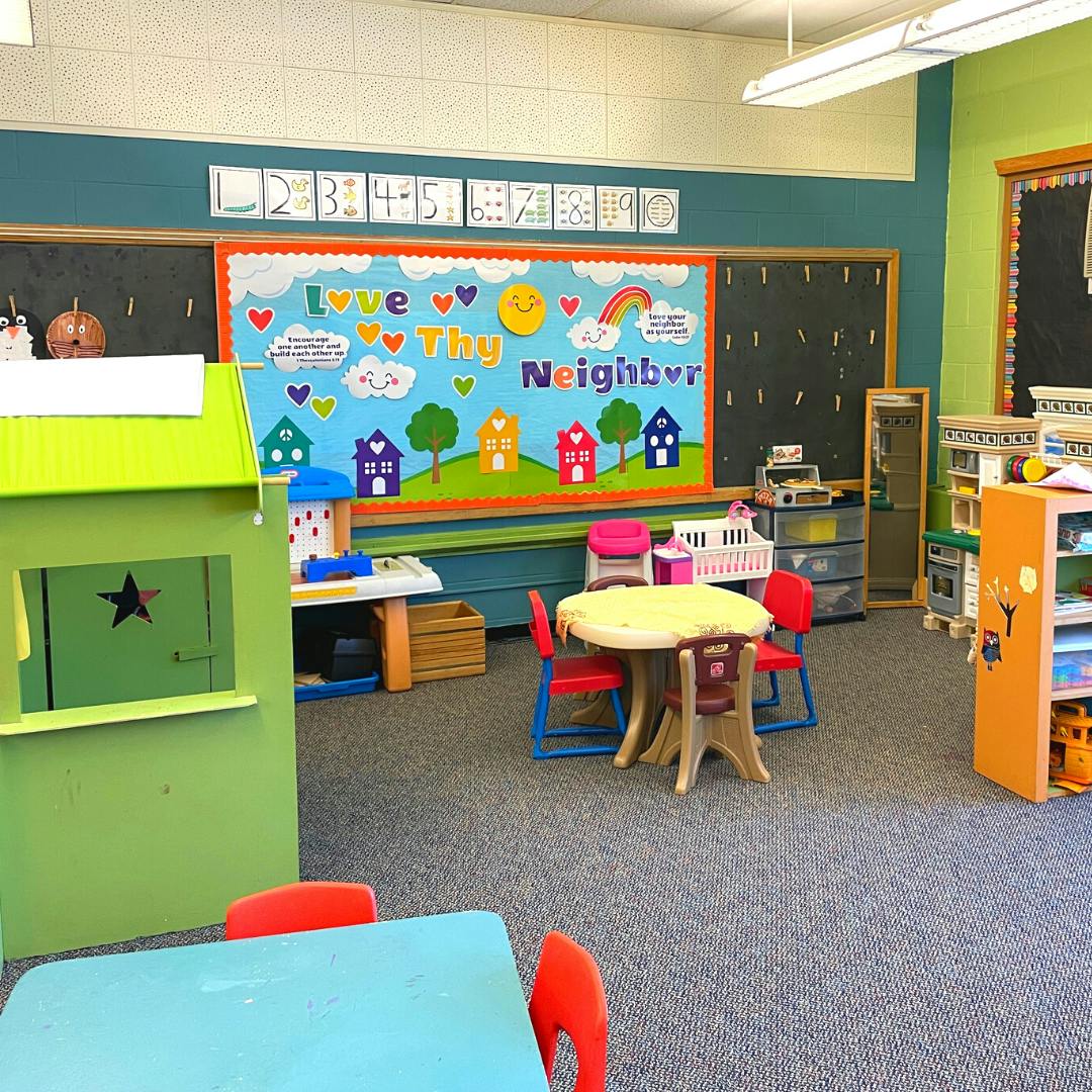 Classroom with playhouse, small tables and chairs, and a bulletin board