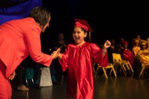 Adult and child in graduation attire shaking hands