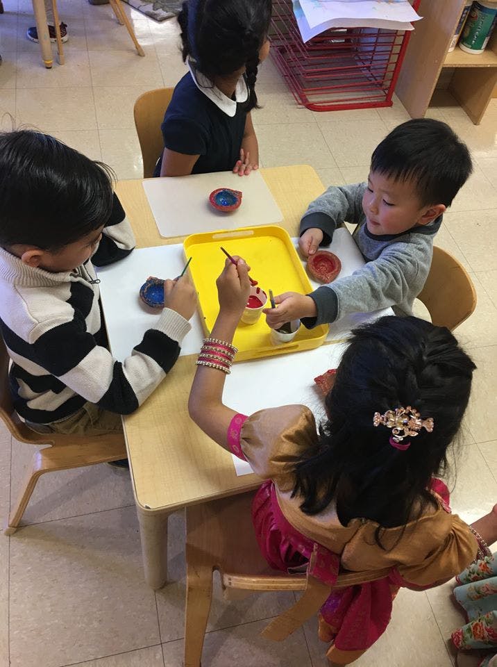 Children painting small objects at a table in a classroom