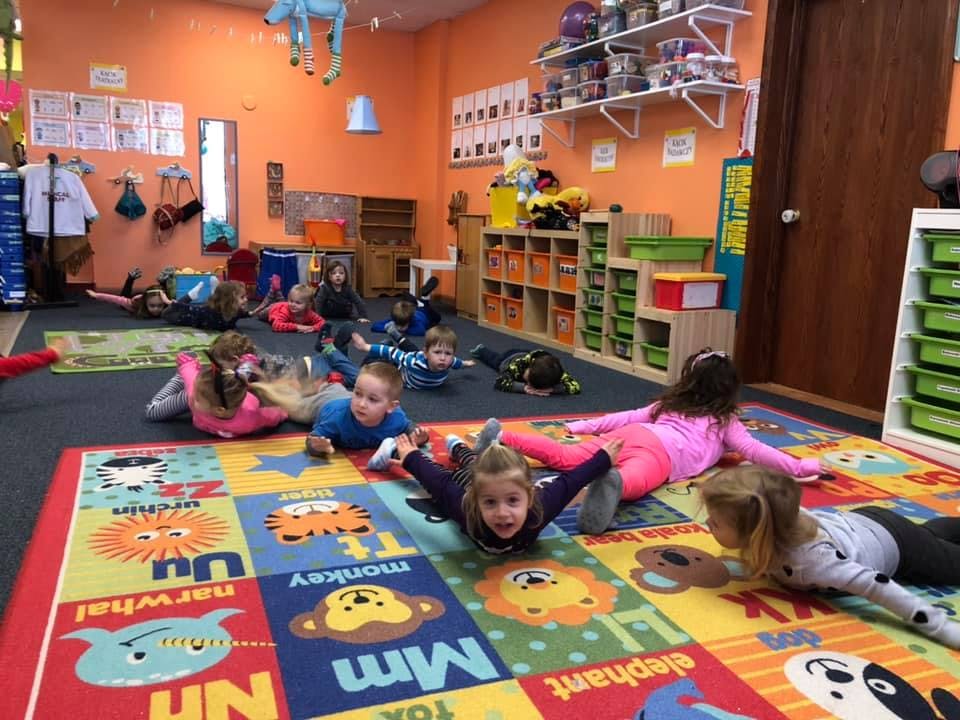 Children lying on their stomachs on a colorful alphabet rug in a classroom