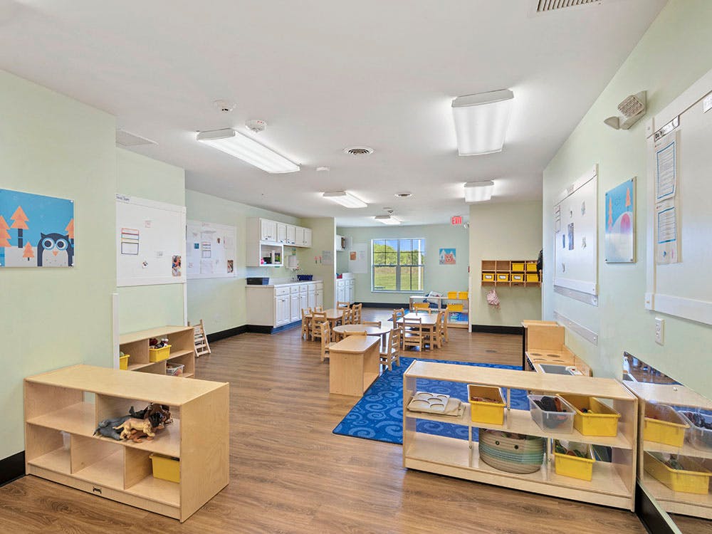 Classroom with small tables, chairs, and shelves with toys and supplies