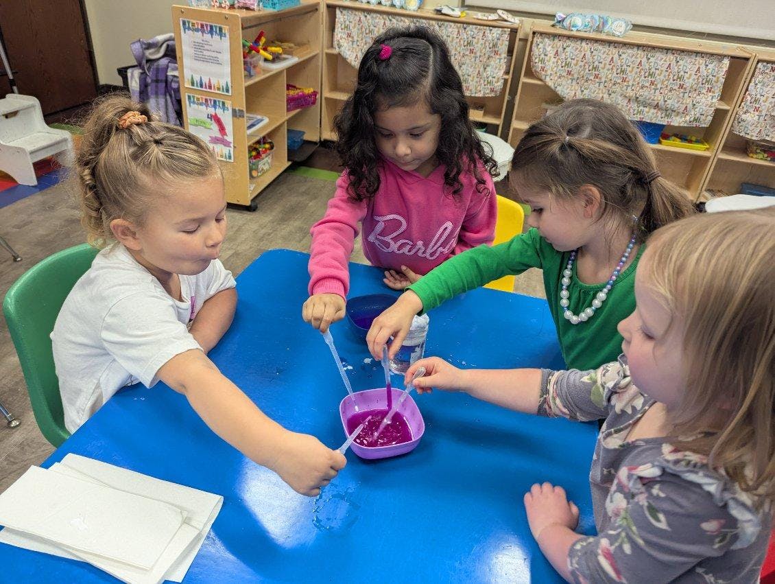Children using droppers to transfer purple liquid into a bowl at a classroom table