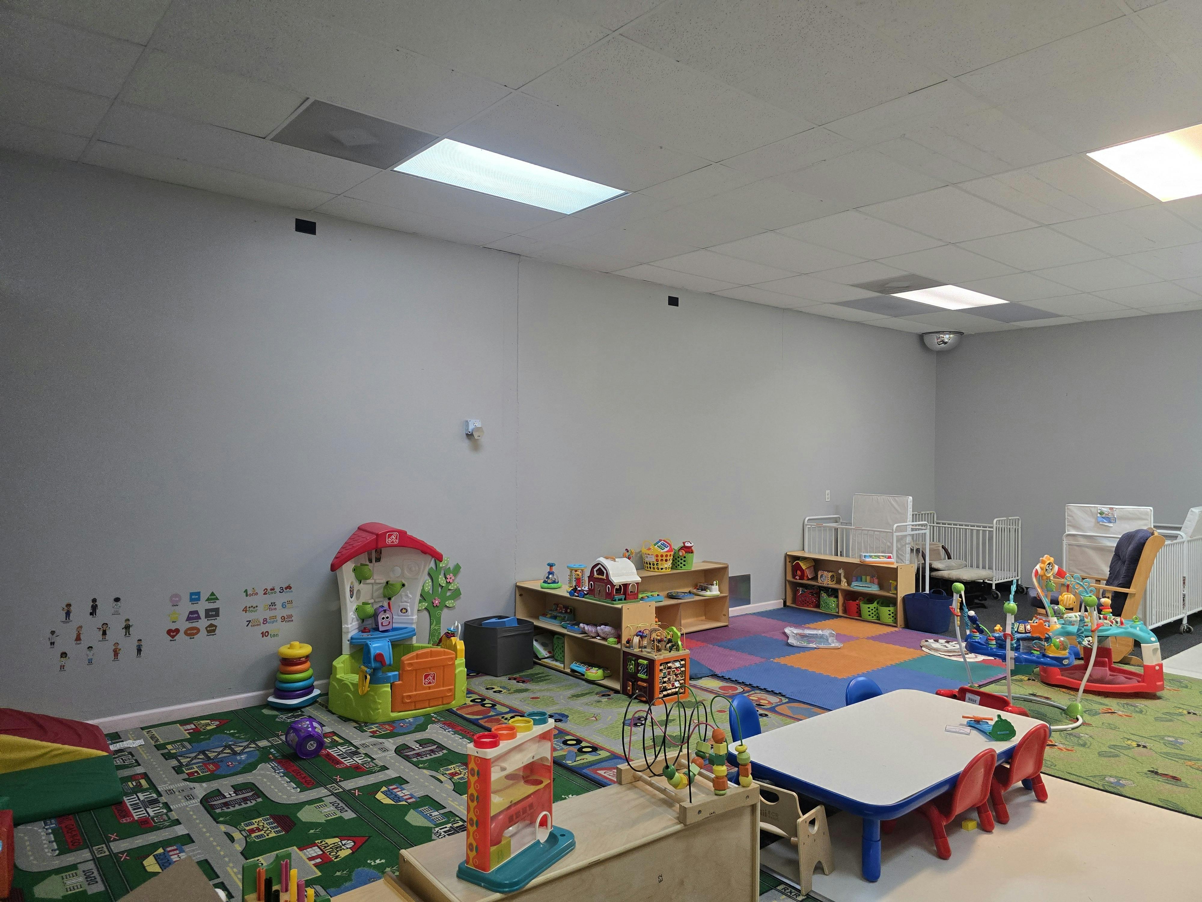 Playroom with toys, small tables, and cribs