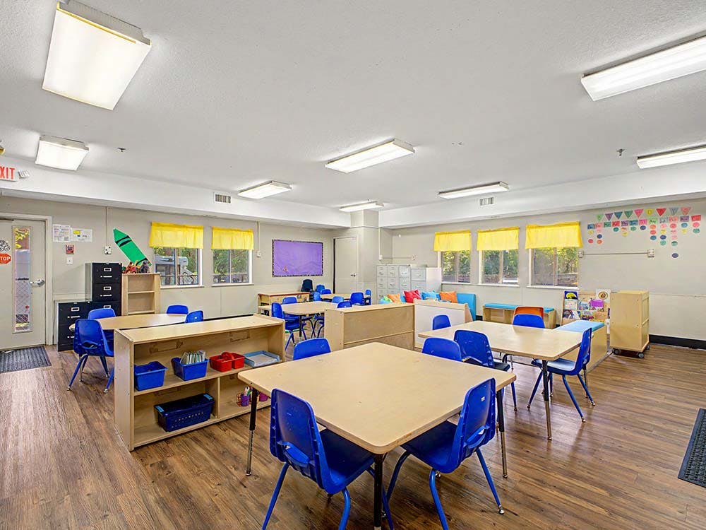 Classroom with small tables and chairs, and bright yellow window valances