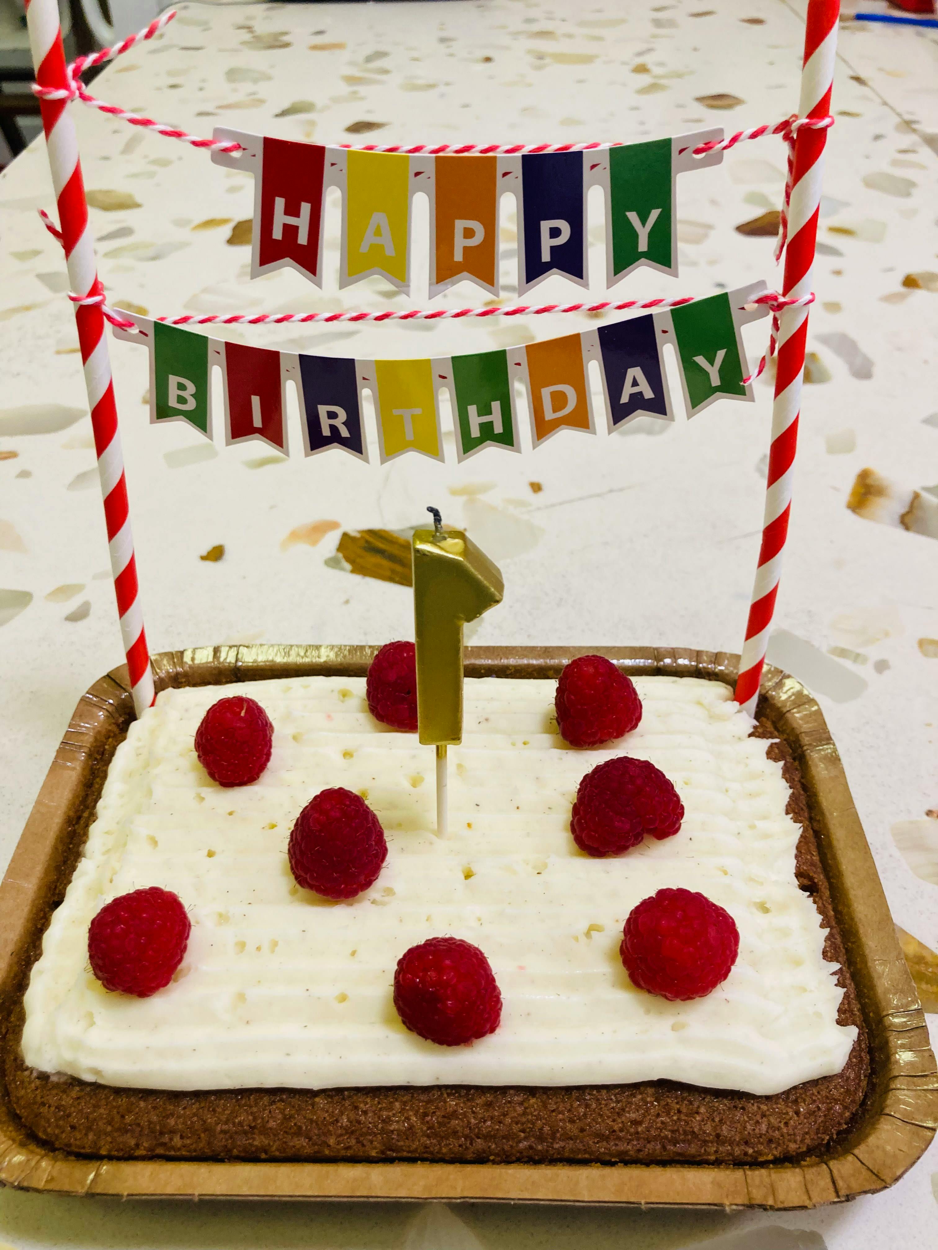 Birthday cake topped with raspberries and a number one candle
