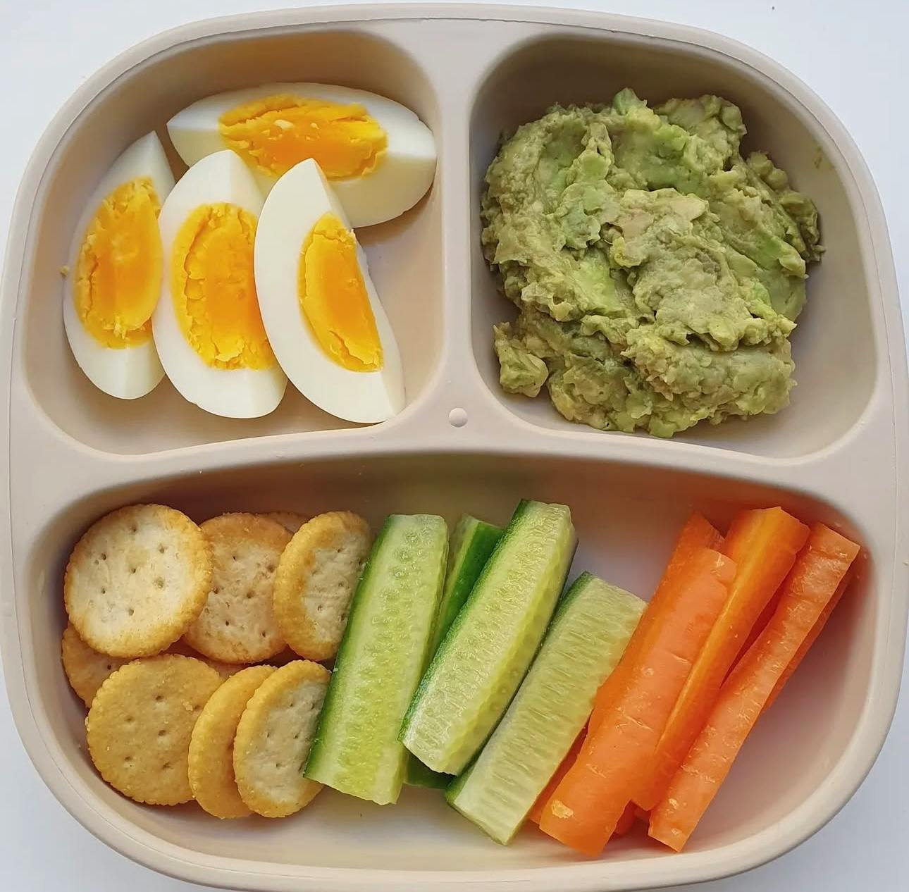 Divided plate with hard-boiled eggs, guacamole, crackers, cucumber, and carrots