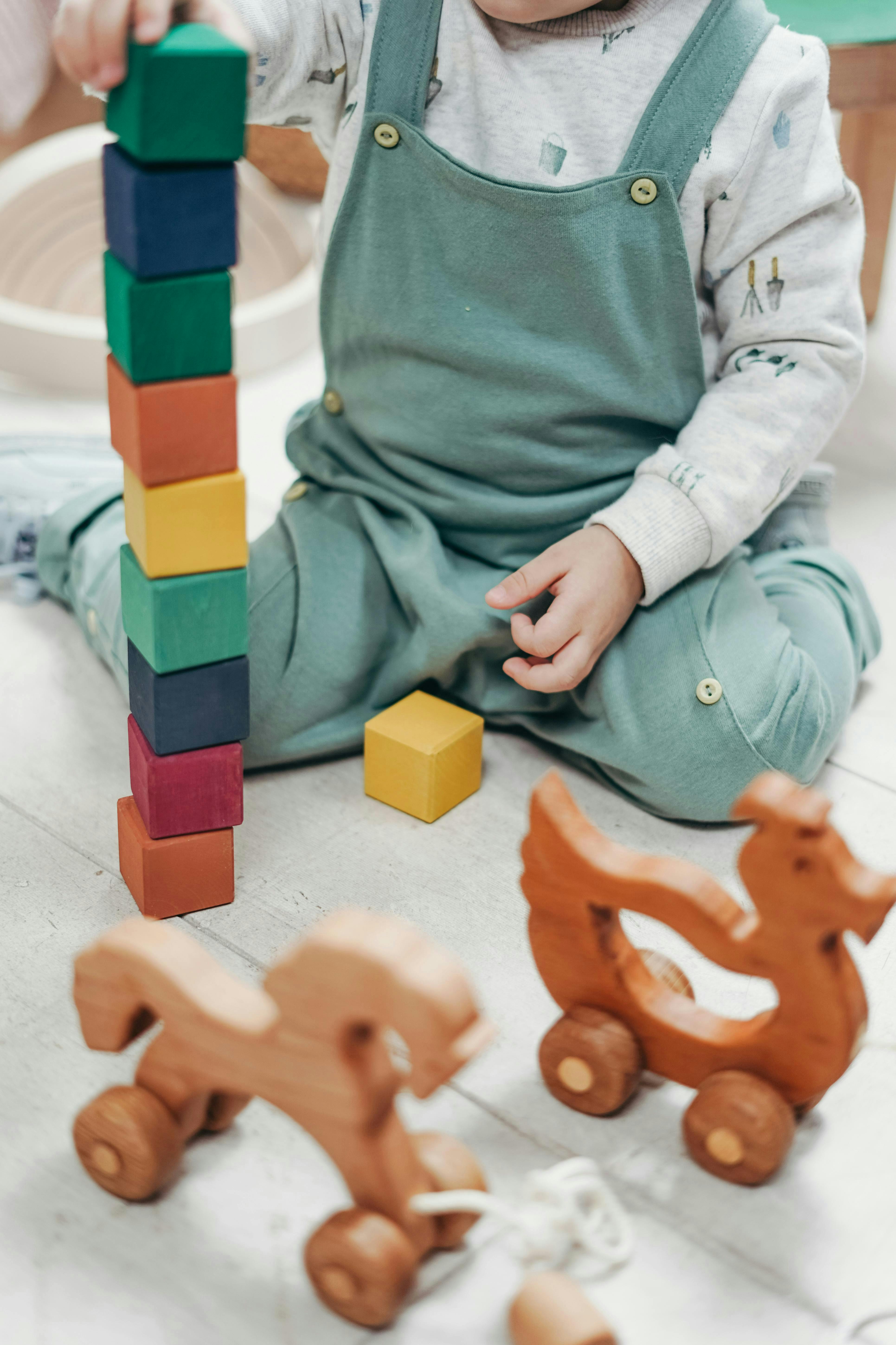 Child stacking colorful blocks on a wooden floor with wooden toys