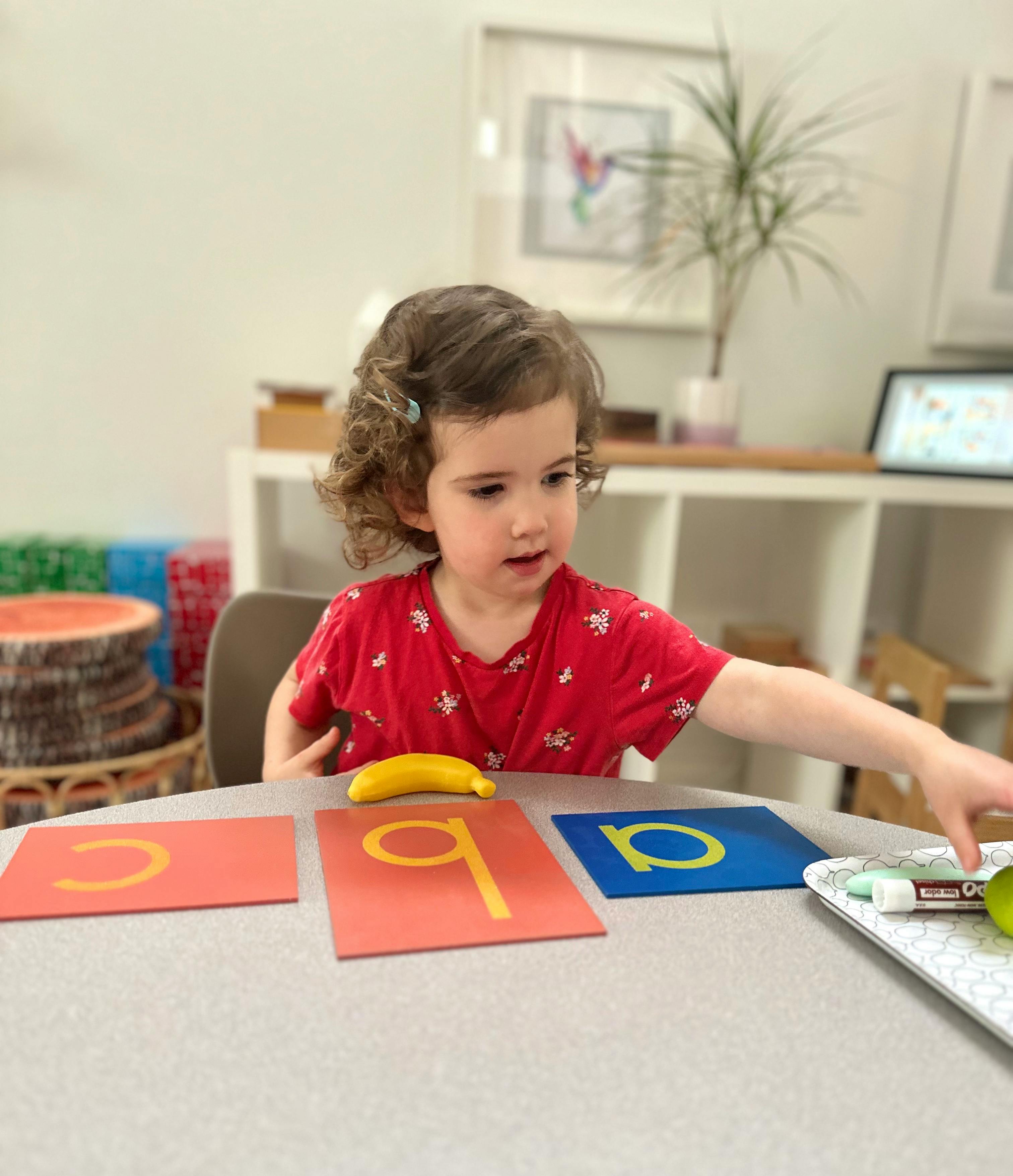 Child at table with alphabet cards and a banana toy