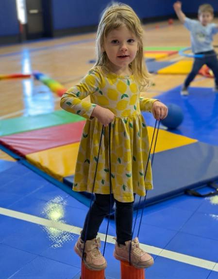 Child standing on small stilts in a gymnasium