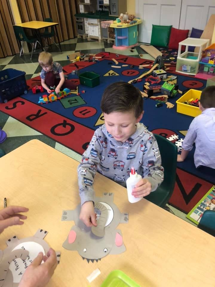 Child holding glue bottle and working on craft at a table