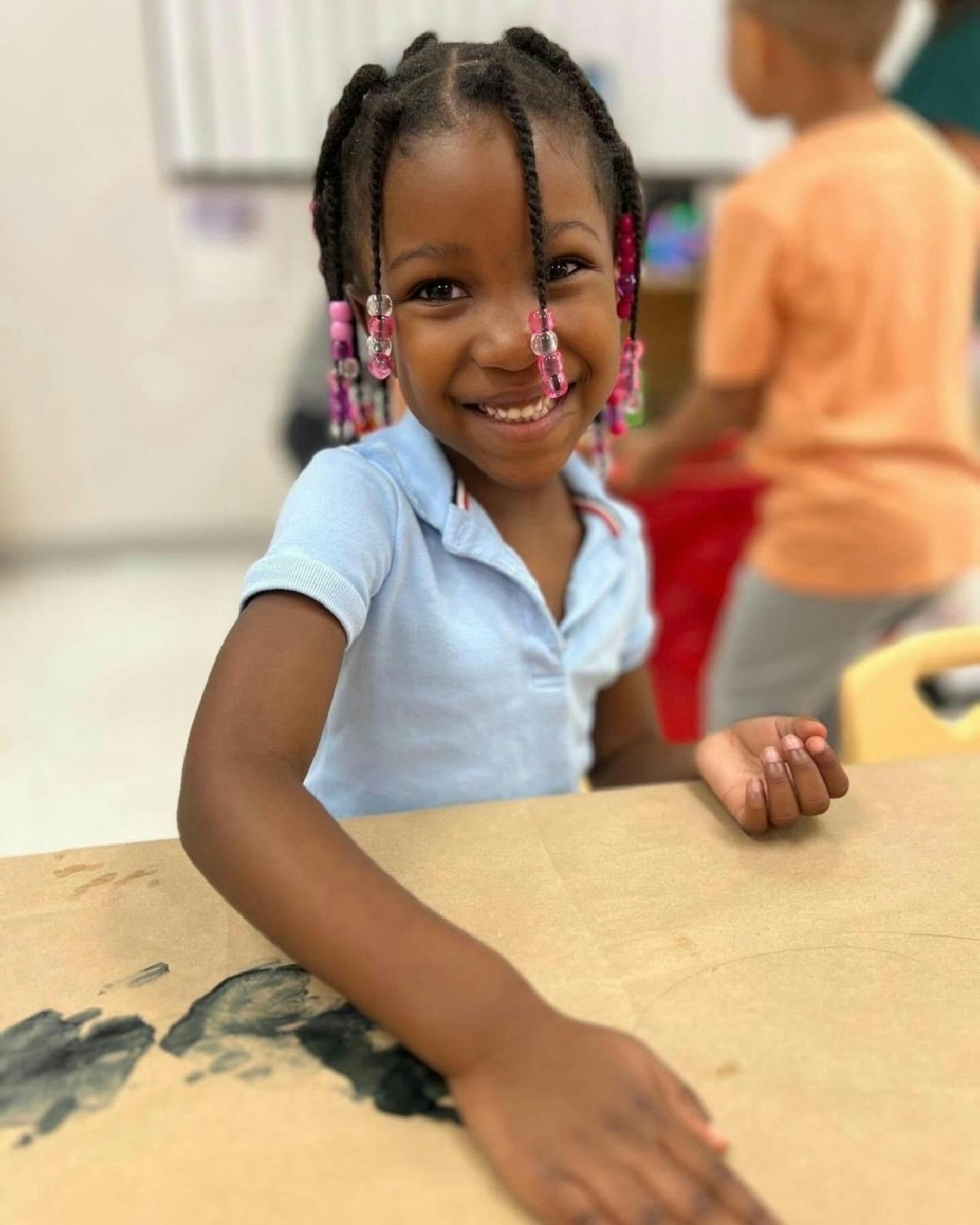 Child with braided hair and beads smiling at a table