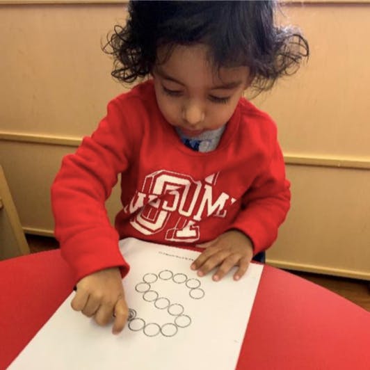 Child tracing a letter S made of circles on a piece of paper