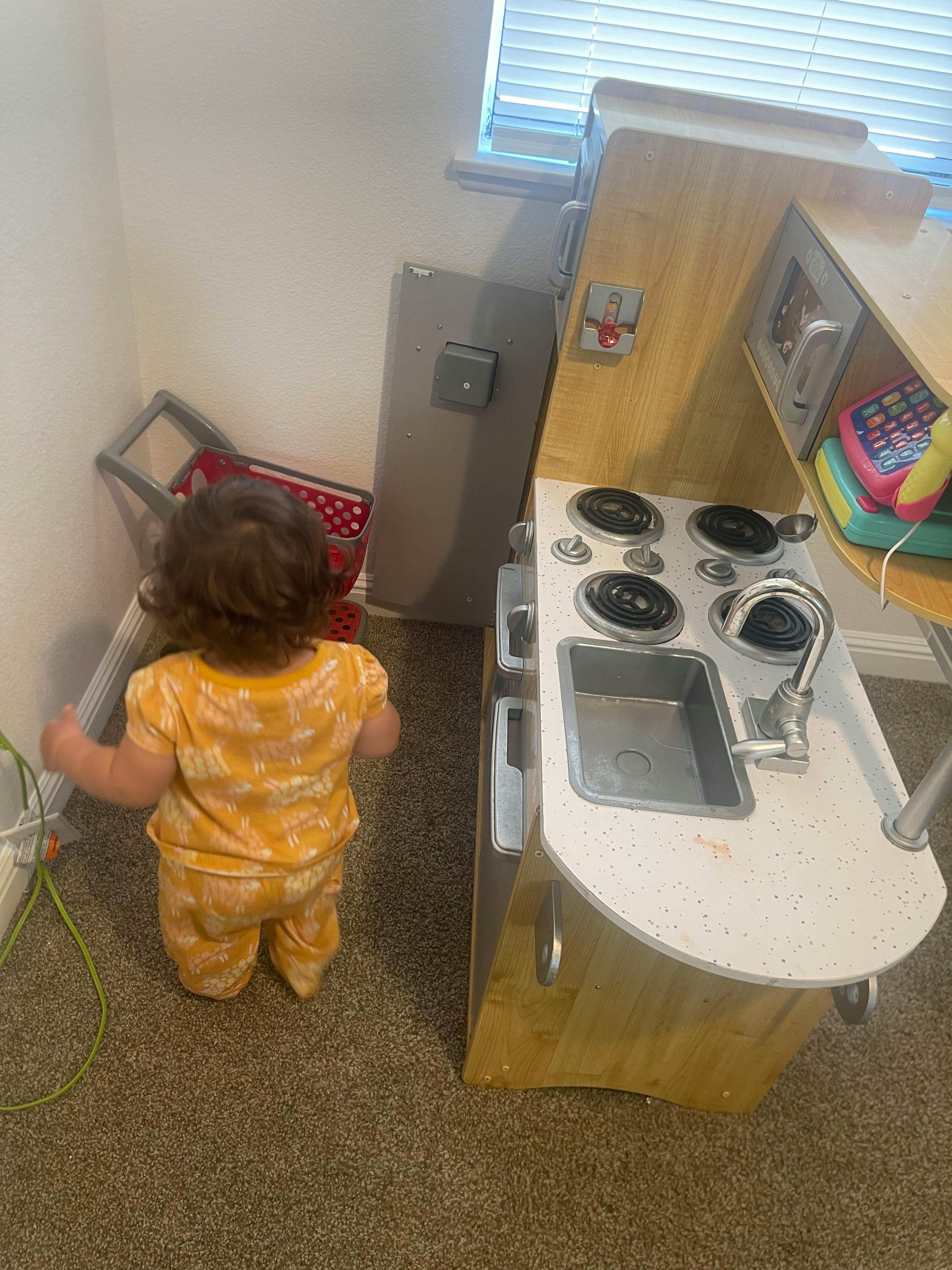 Child playing with a toy shopping cart and a toy kitchen