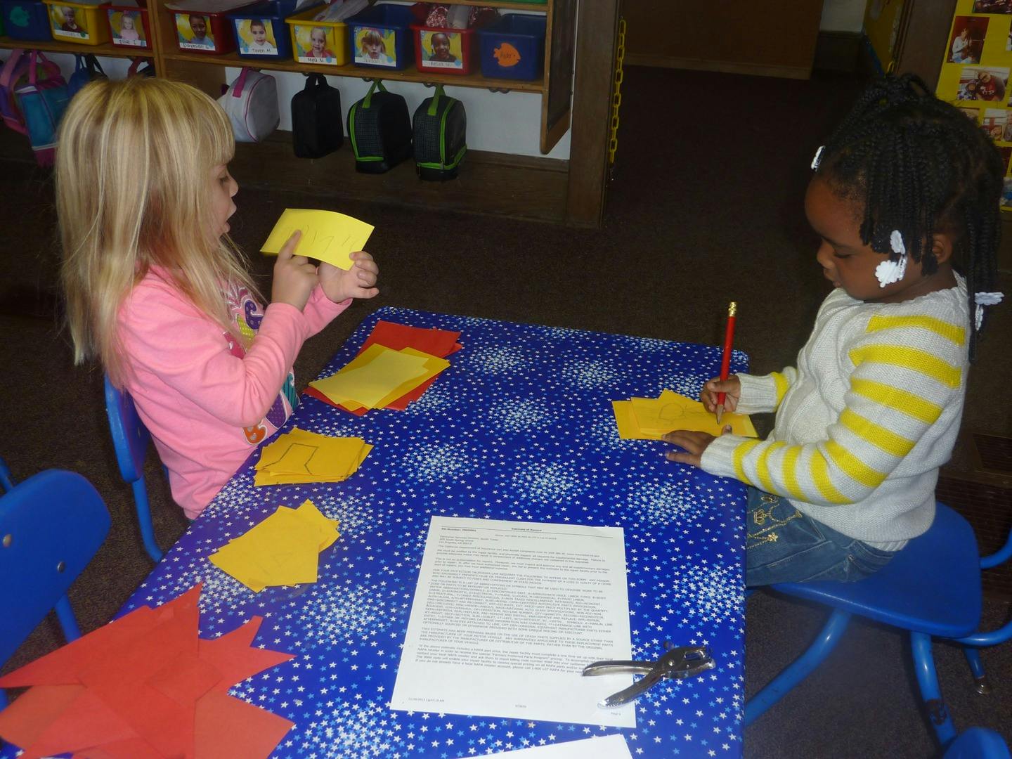 Two children sitting at a table with paper and writing utensils