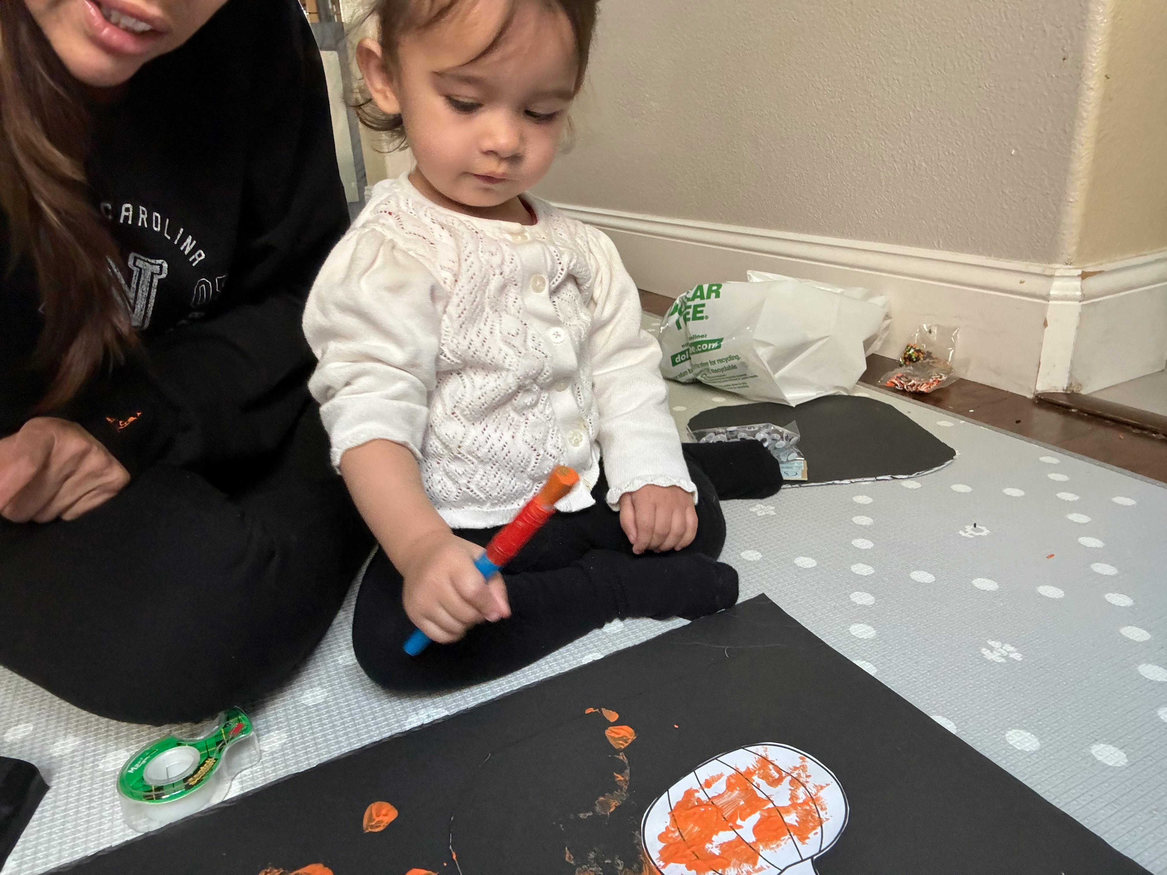 Child and person sitting on floor, child painting on black paper