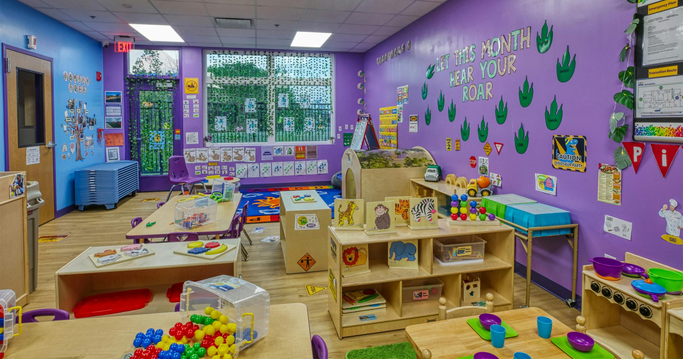 Colorful playroom with toys, small tables, and purple walls with dinosaur decor