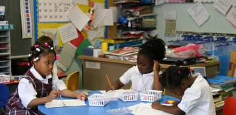 Three children working at a table in a classroom