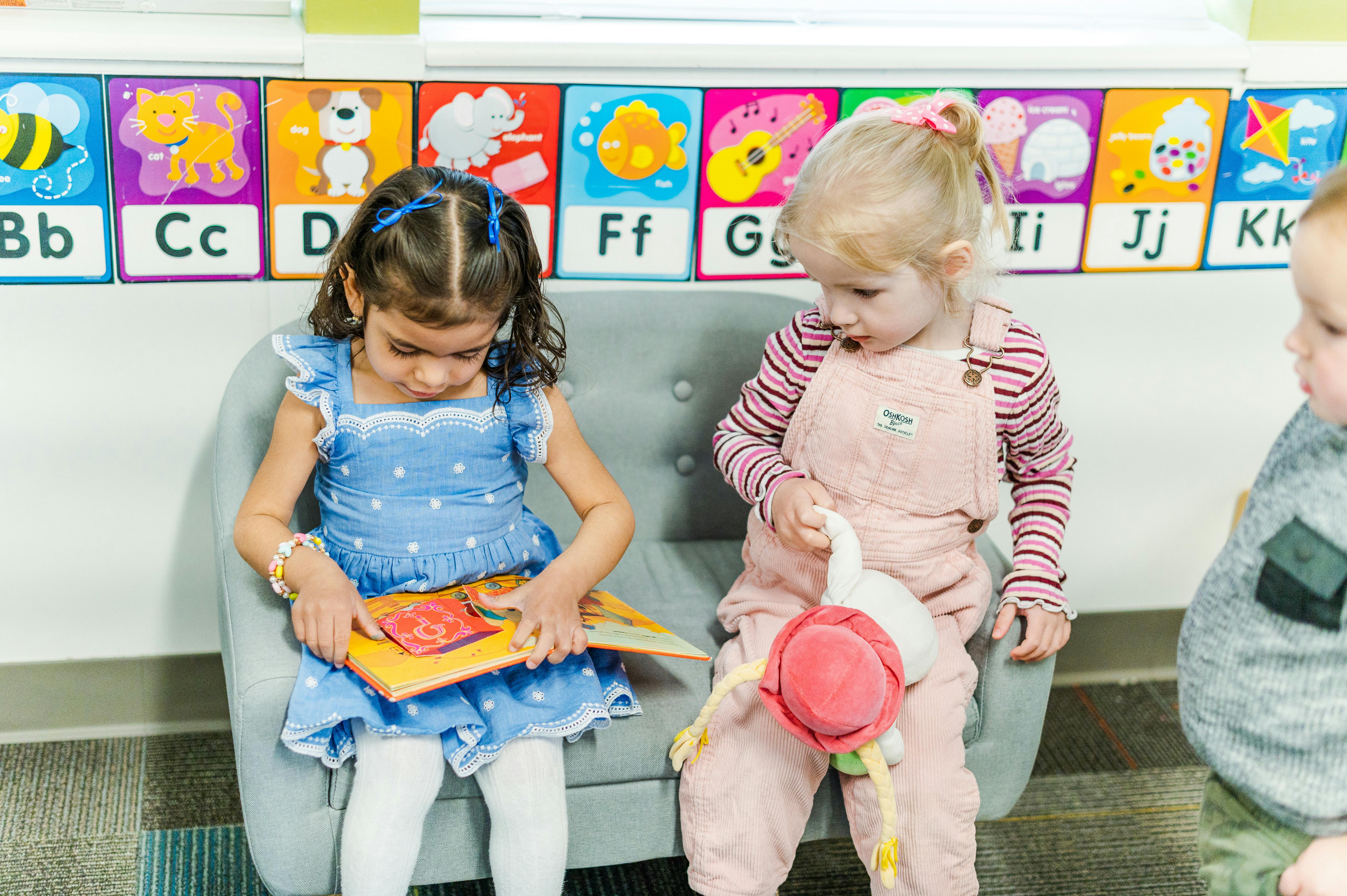 Two children sitting on a couch, one reading a book