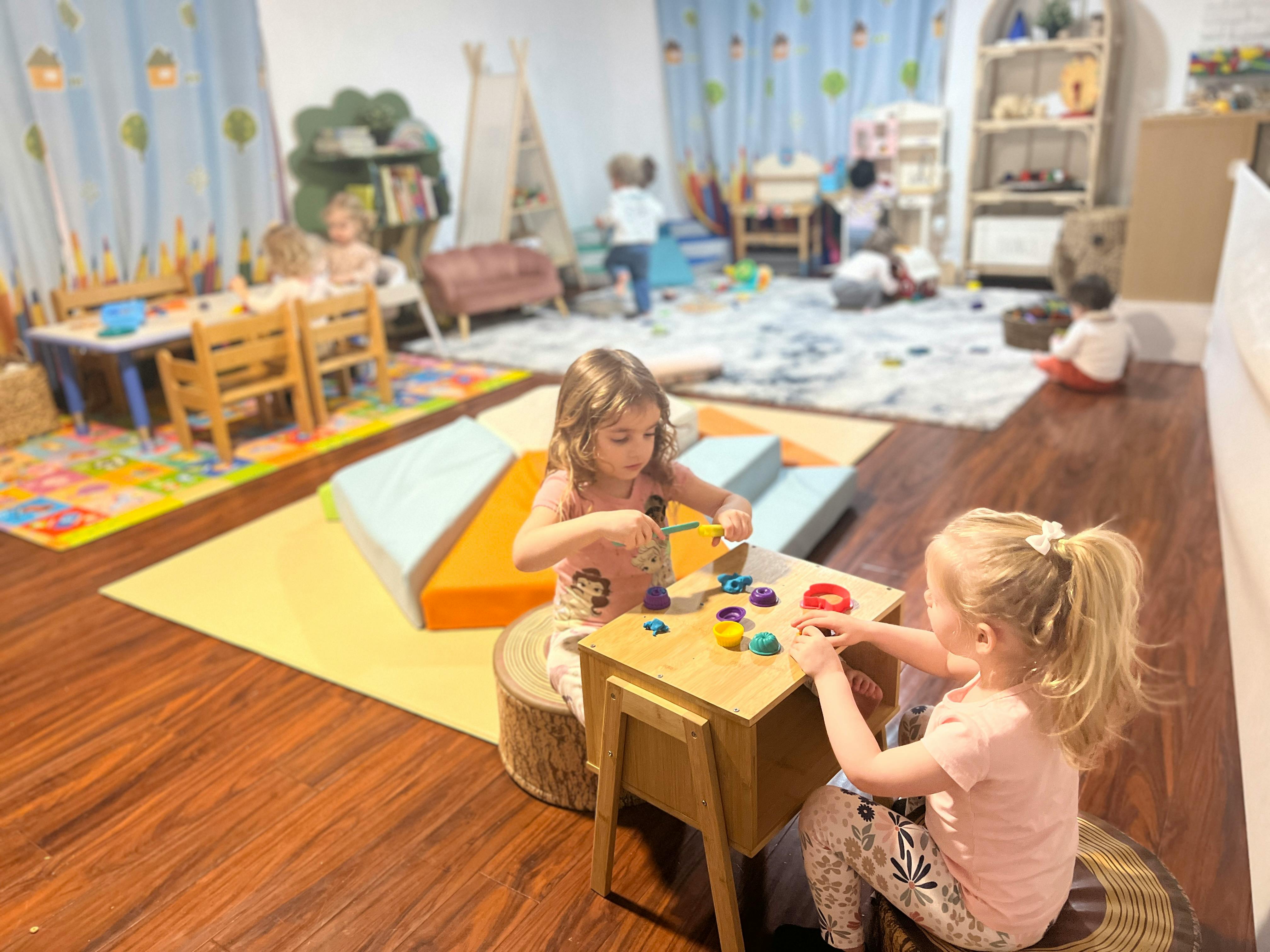 Two children playing with small objects at a table in a classroom