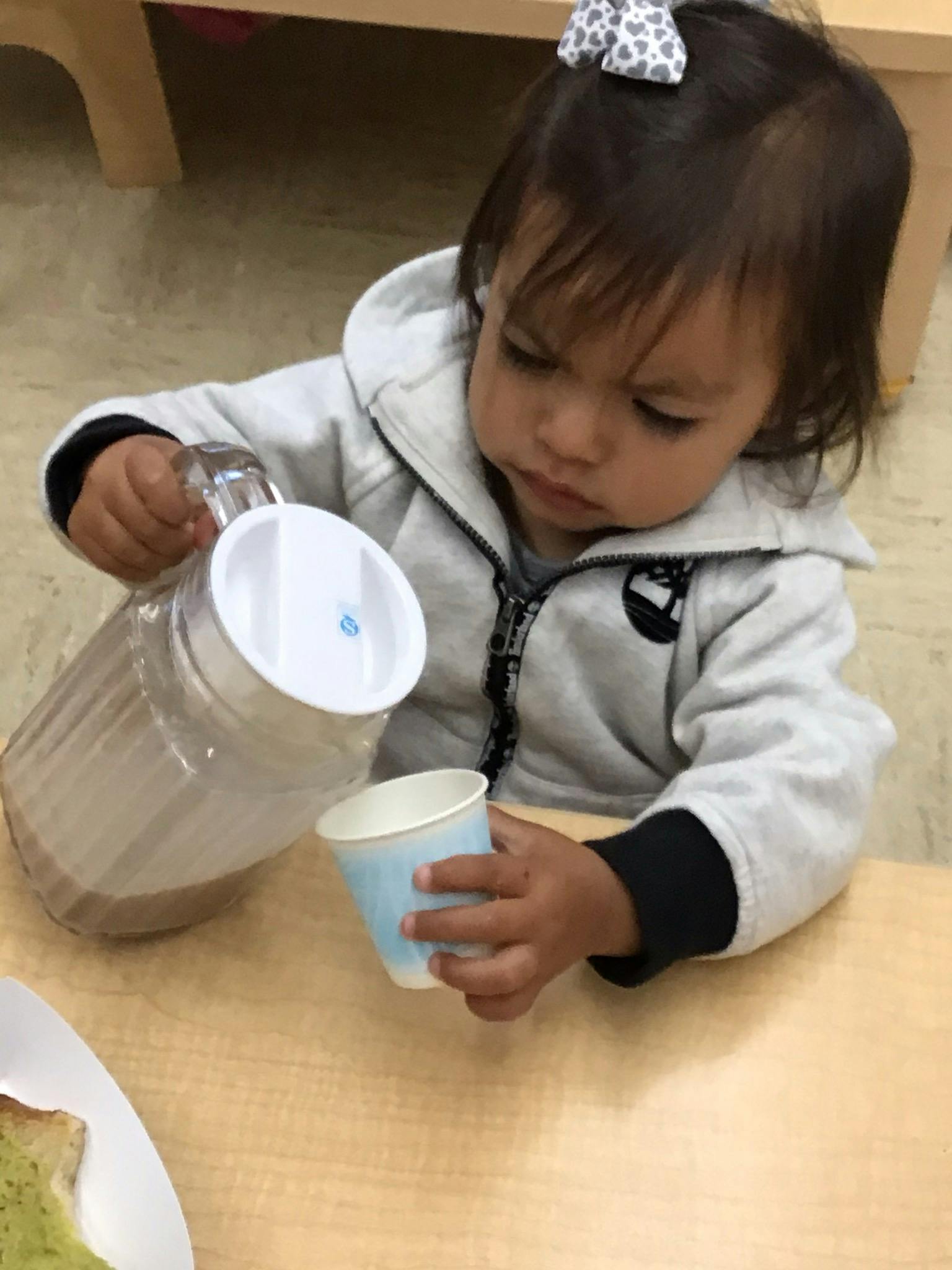 Child pouring liquid from a pitcher into a cup