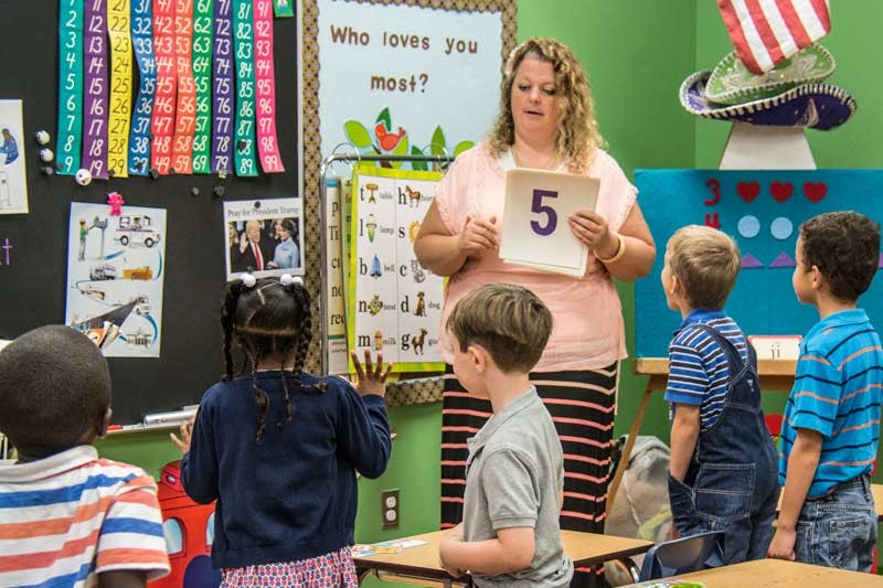 Person holding up a number 5 card to children in a classroom