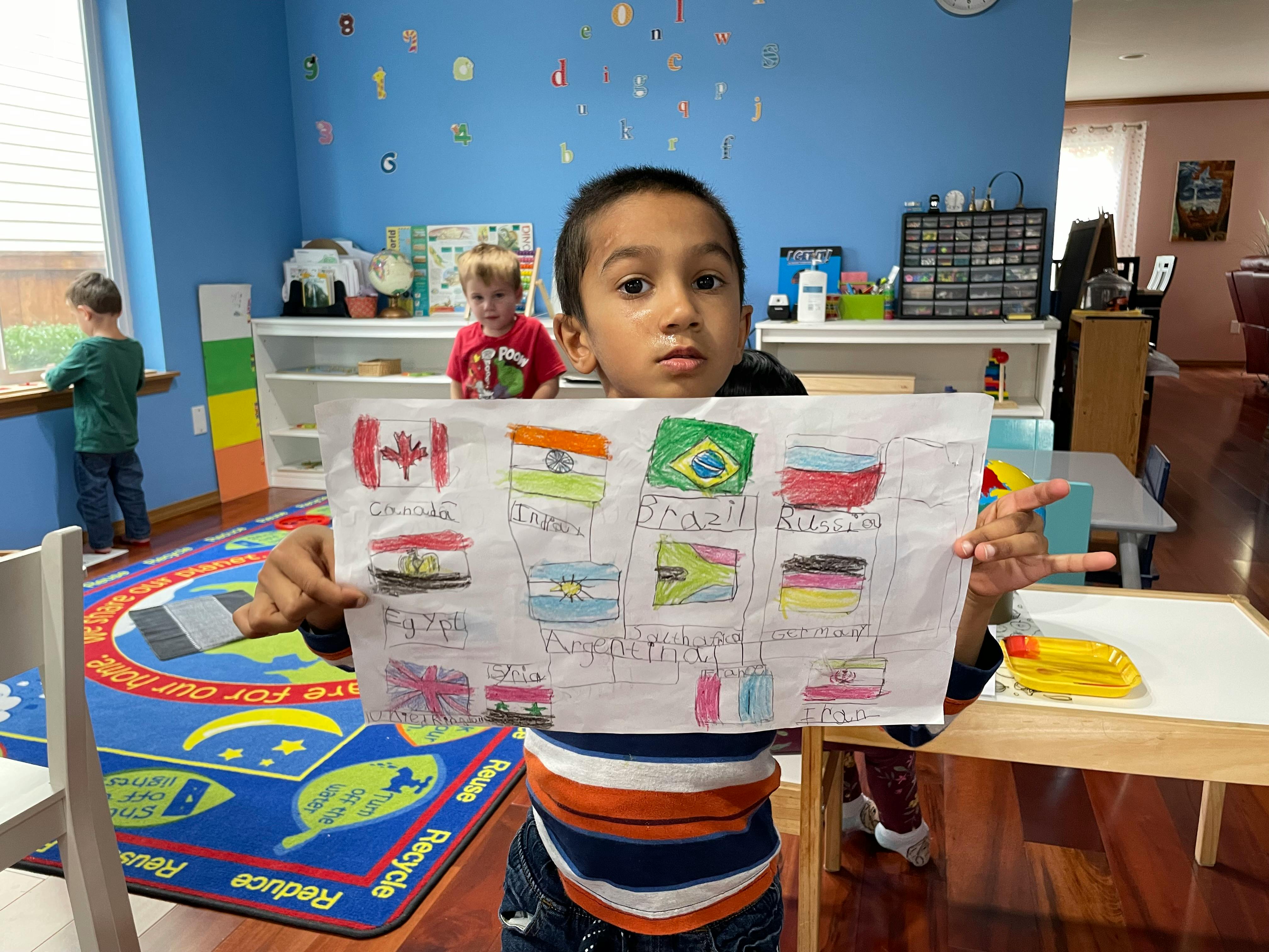 Child holding up a drawing of flags in a classroom