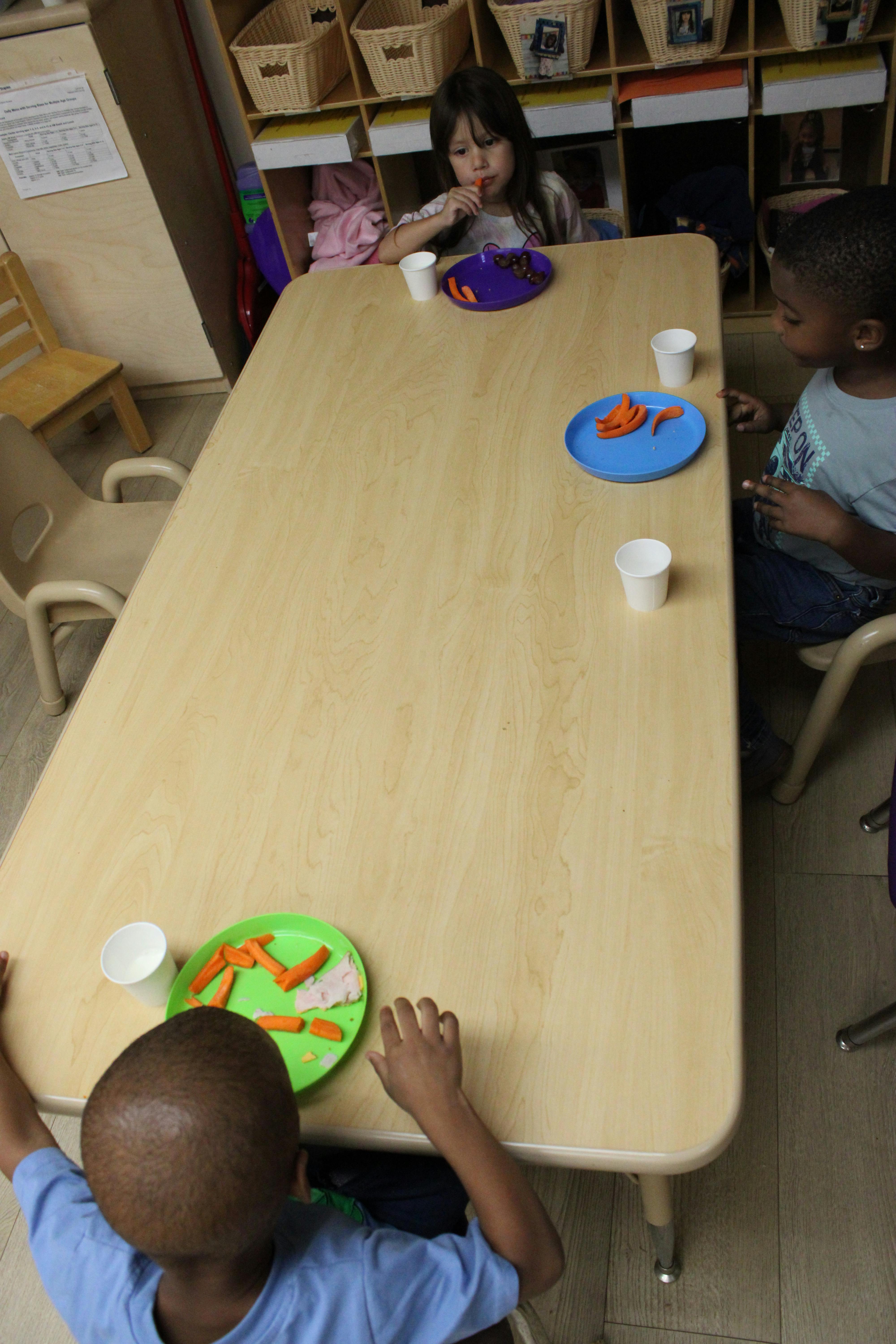 Three children sitting at a table with plates of snacks