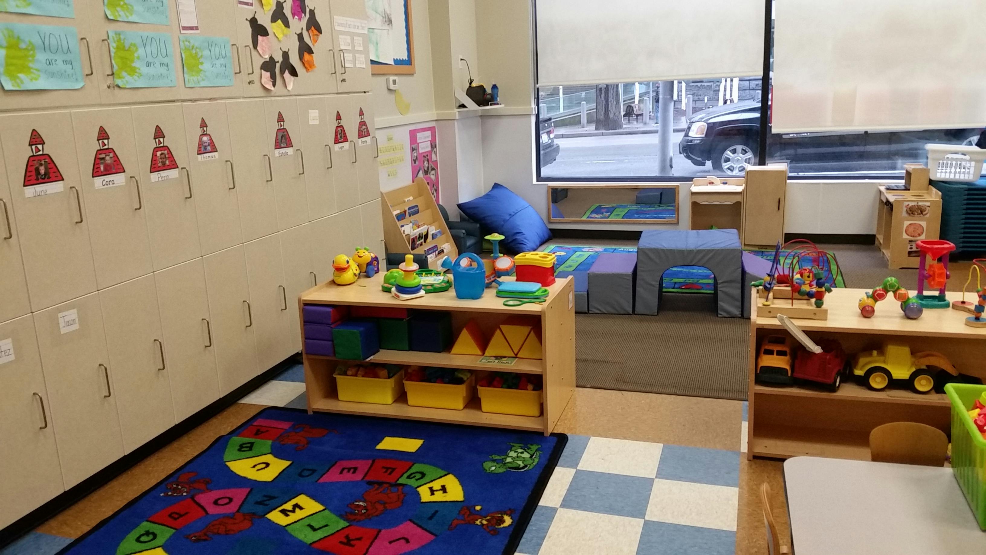 Playroom with children's artwork on lockers, colorful rugs, and various toys