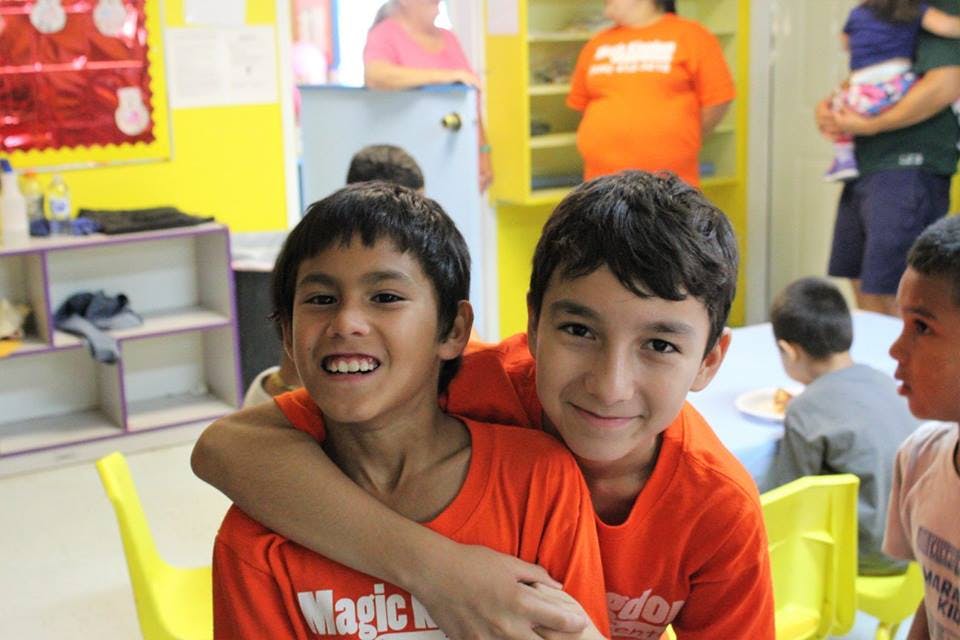 Two children in orange shirts smiling, one with arm around the other
