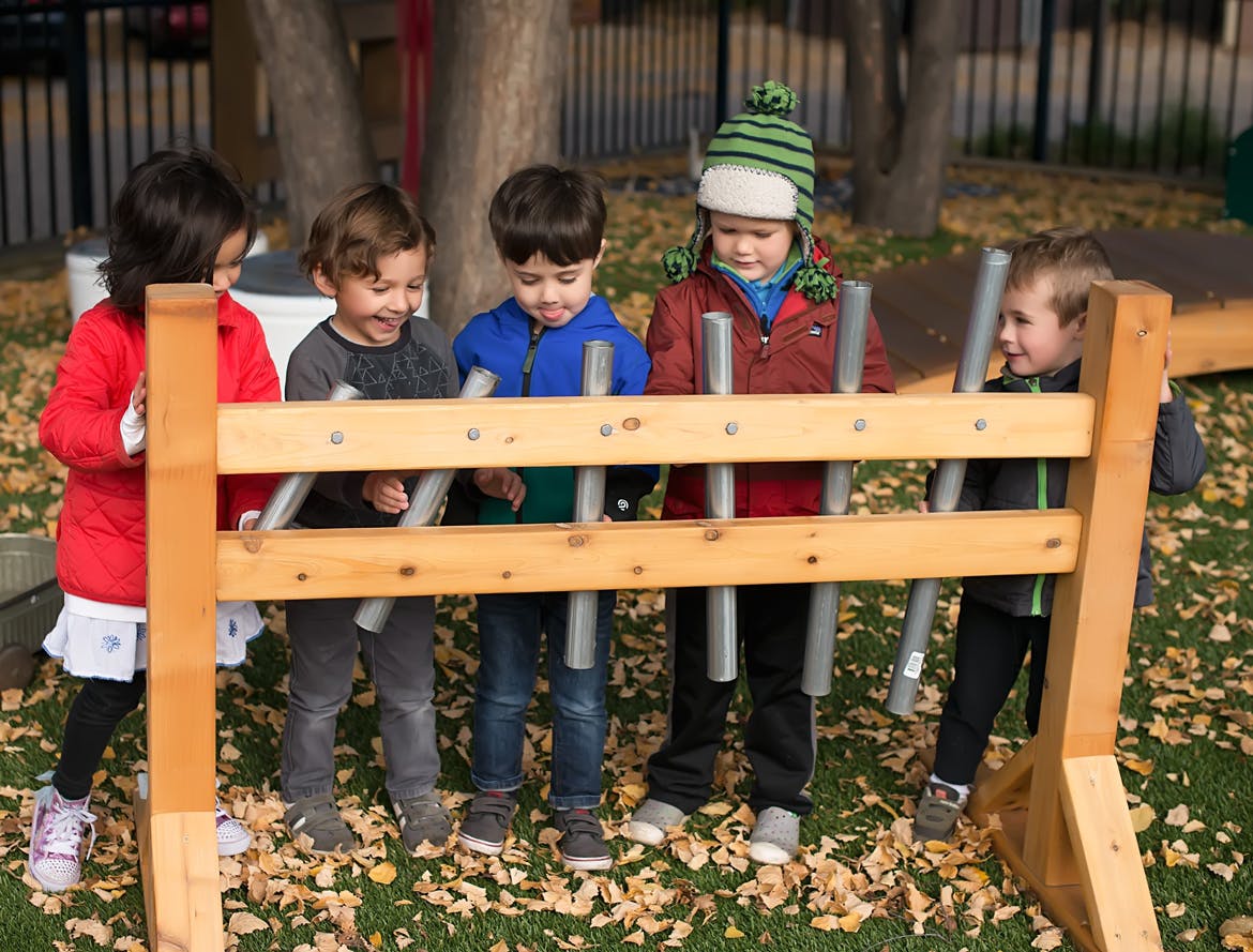 Four children playing with a wooden and metal outdoor musical instrument