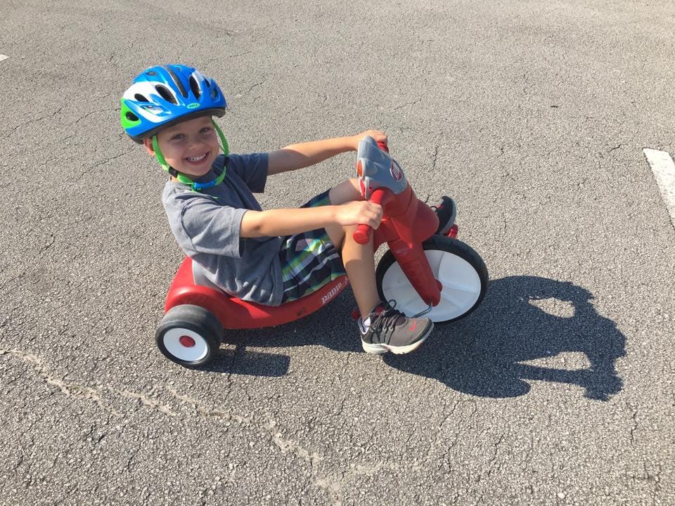 Child in a helmet riding a red tricycle