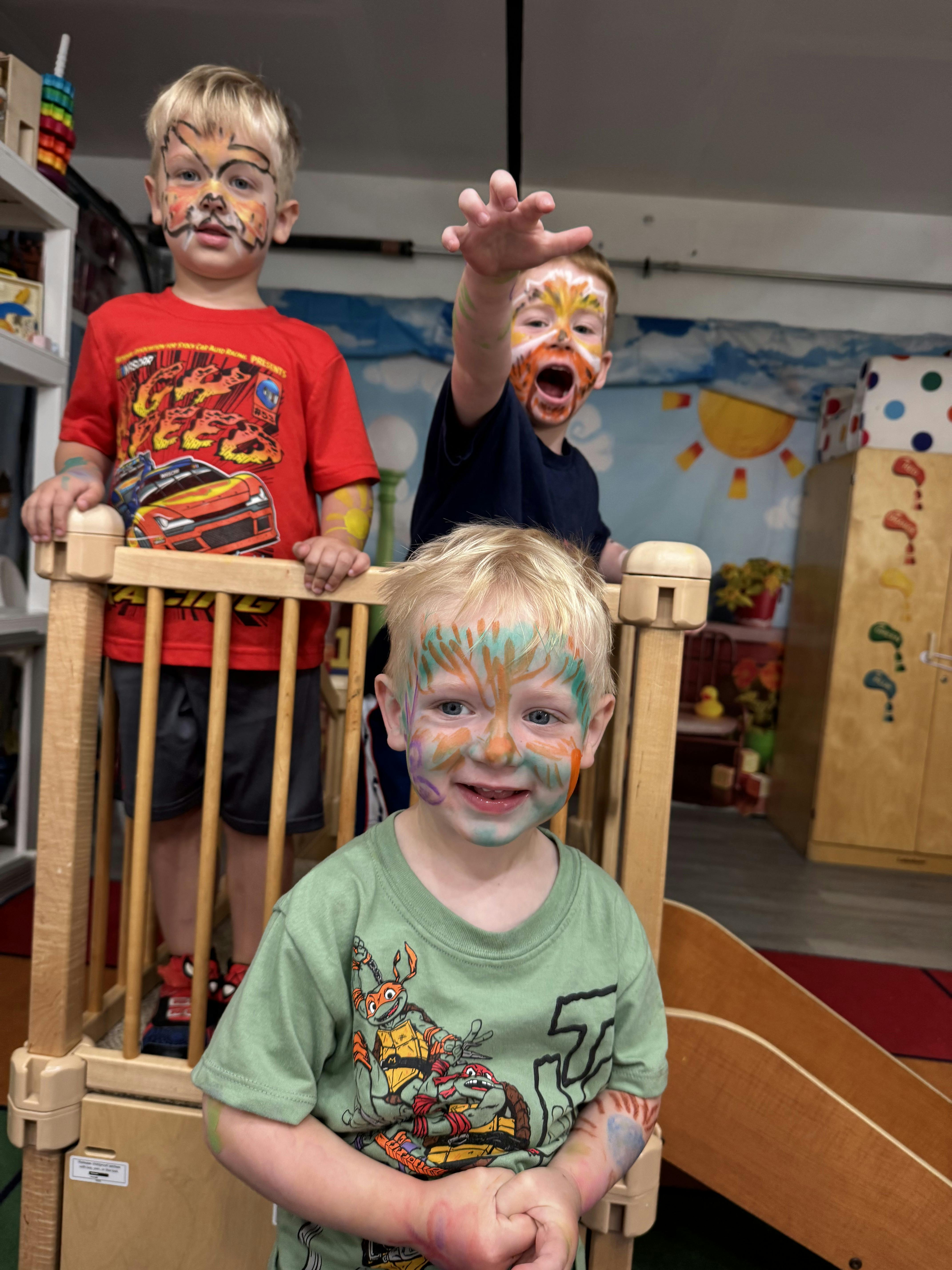 Three children with face paint standing on a small indoor play structure